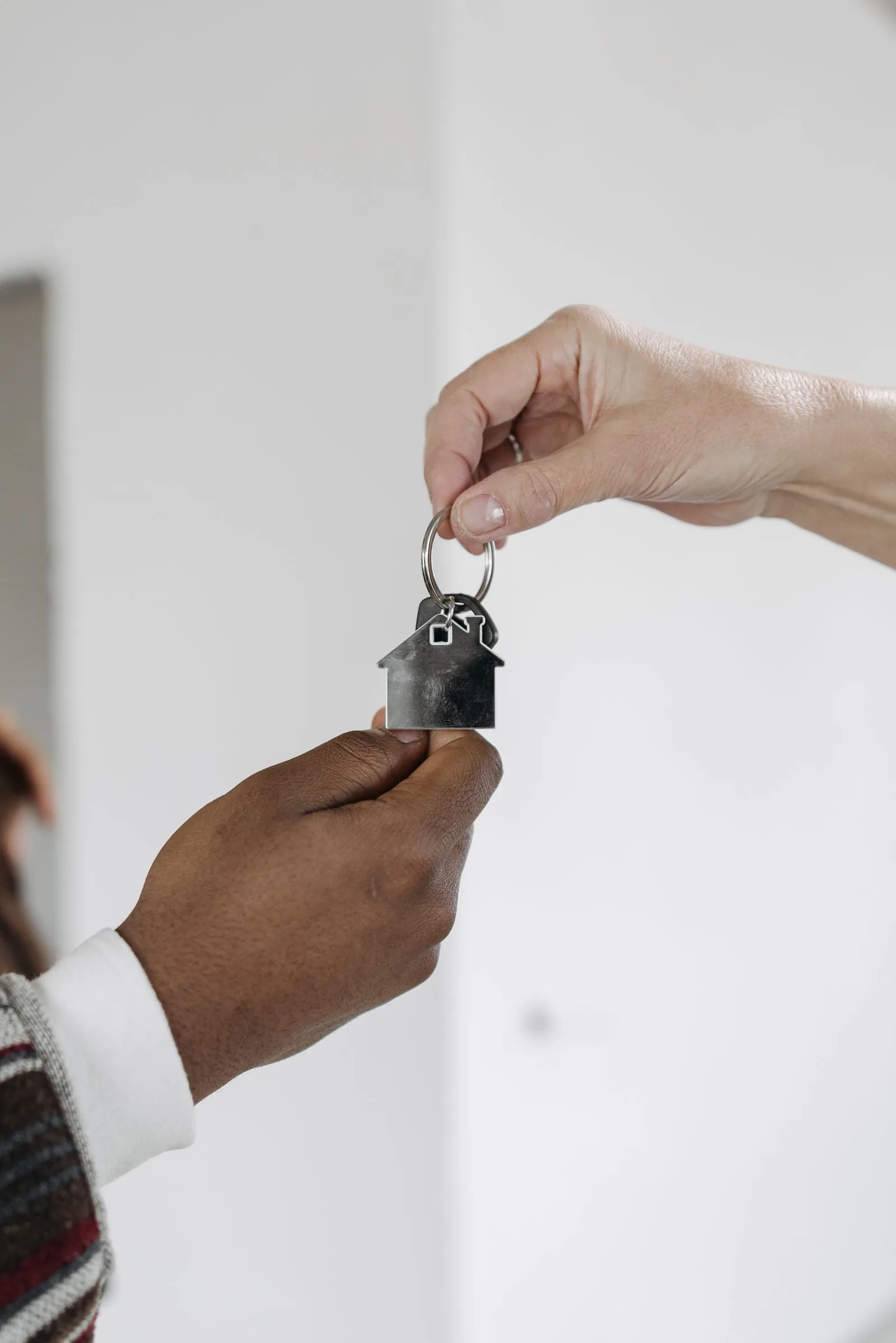A key with a house-shaped keyring being handed over.