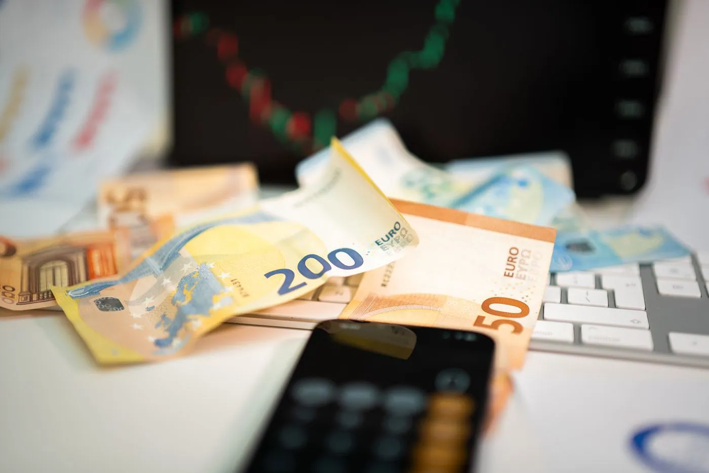 Notas de euro e telemóvel sobre uma mesa de trabalho.