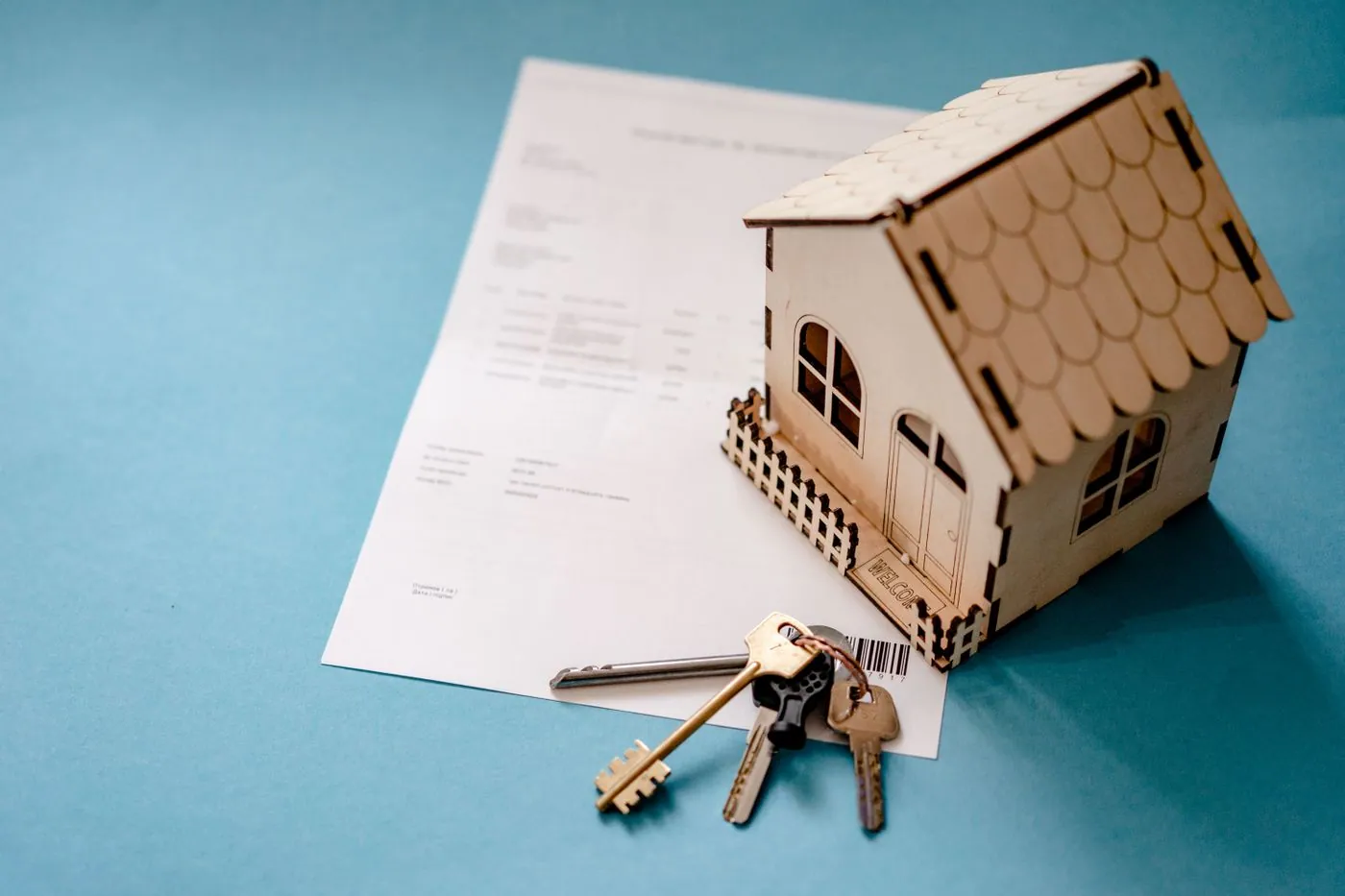 Miniatura de casa em madeira, chaves e contrato sobre uma mesa.