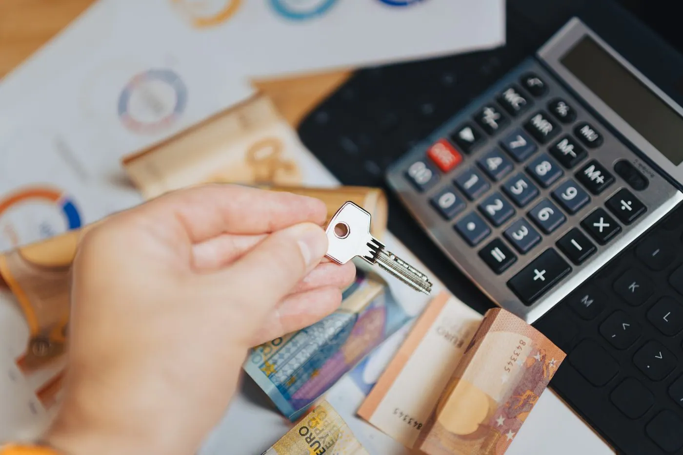 A hand holding a key above euro banknotes and a calculator.