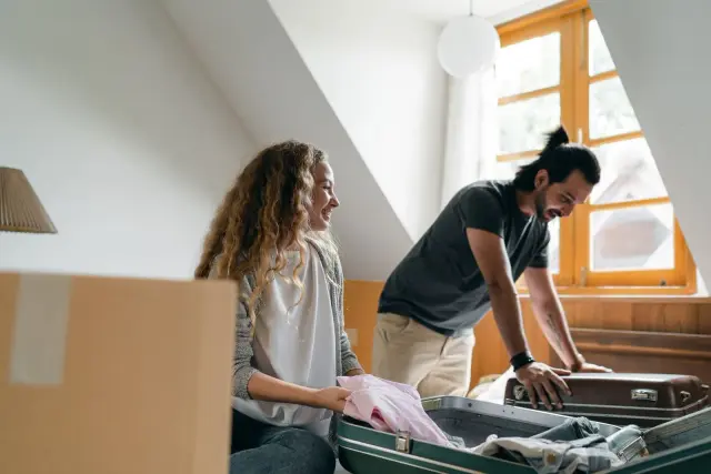 Casal a organizar malas e caixas de uma mudança numa casa.
