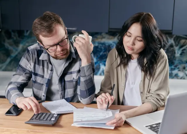 Casal a rever o orçamento doméstico com contas, calculadora e portátil.