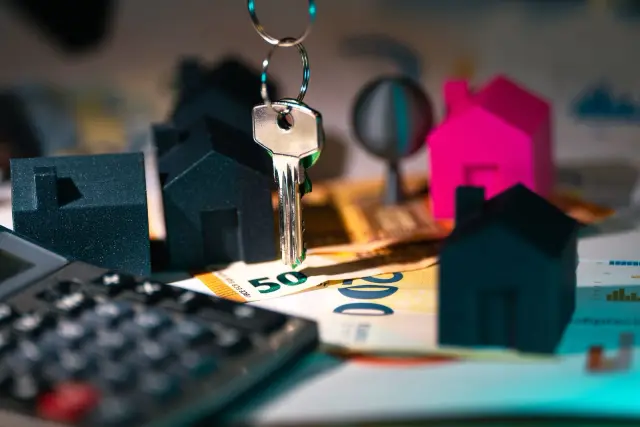 Notas de euro, chaves e miniaturas de casas sobre uma mesa.